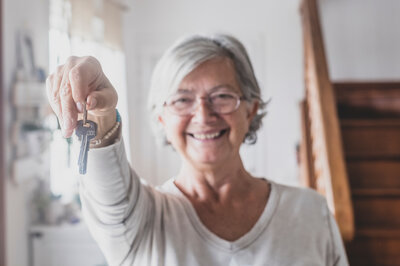 Seniorin hält einen Schlüssel in die Kamera | © Adobe Stock