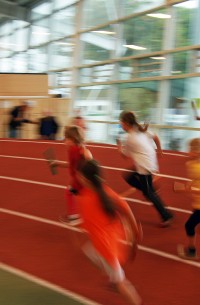 Sie sehen Kinder in einer Leichtathletikhalle beim Staffellauf.