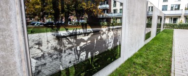 Sie sehen auf der großen Spiegelflächen einer Sichtschutzmauer das historische Foto eine Gruppe von Kindern. Es gehört zum Kunstprojekt  "Zeitgeister" von Arne Lösekann.